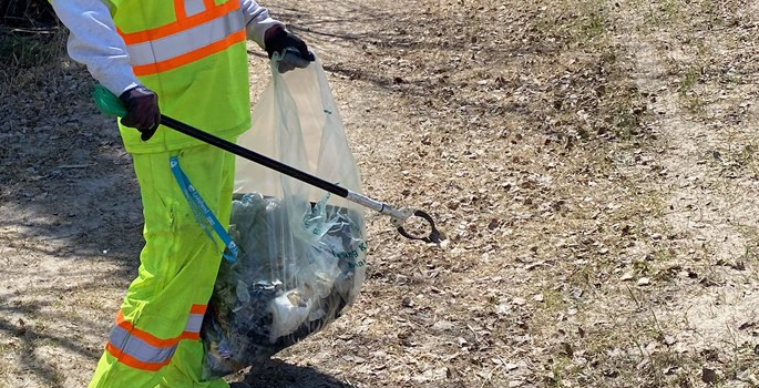 person in bright coloured clothing picking up garbage on the roadside